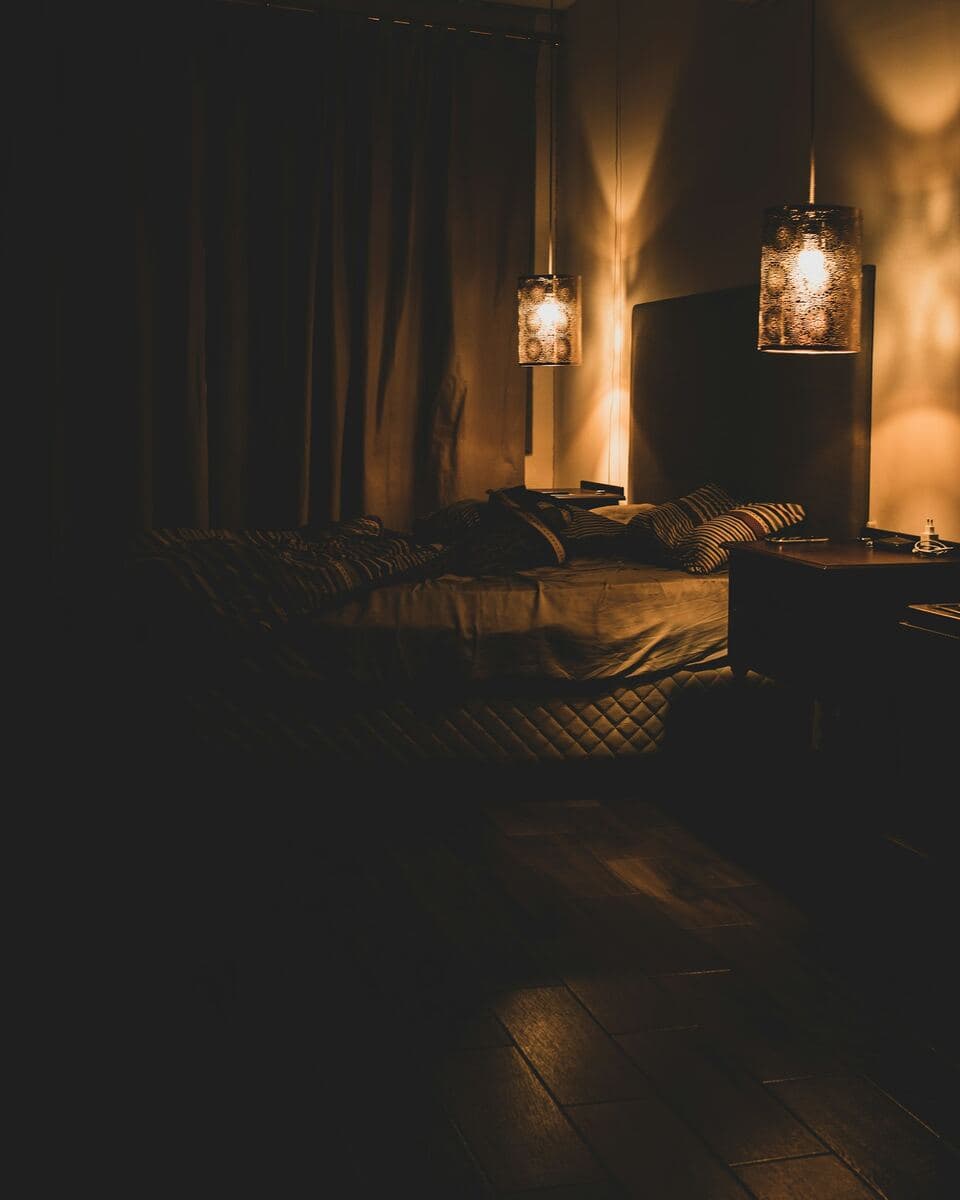 Dim bedroom lit by two warm bedside lamps